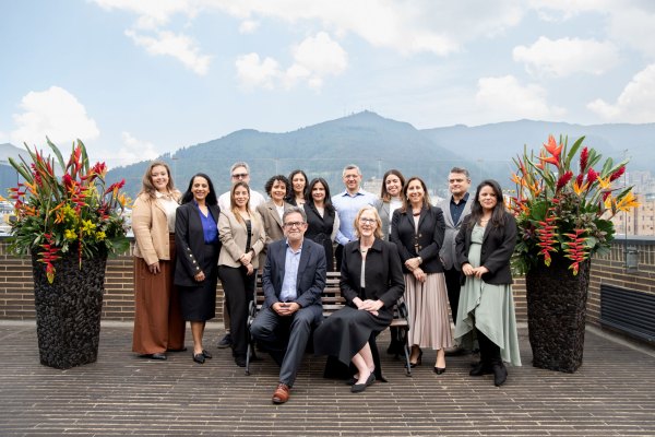 Heather Gerken poses next to Javier Ciurlizza and 11 other Ford Foundation team members on a terrace with scenic mountains in the background. Colorful floral arrangements frame the scene.